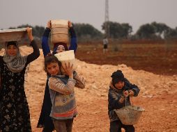 Varios niños transportan agua en recipientes improvisados, en un campo de refugiados sirios. AFP/A. Watad