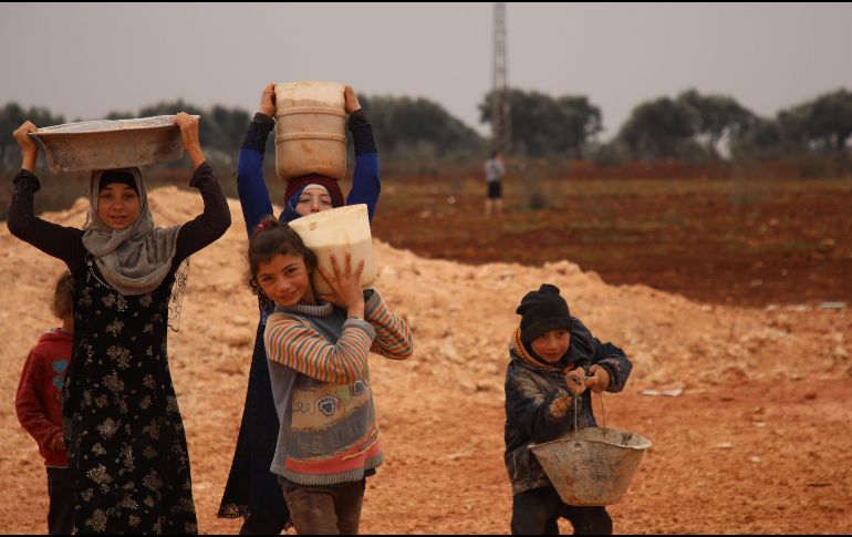 Varios niños transportan agua en recipientes improvisados, en un campo de refugiados sirios. AFP/A. Watad