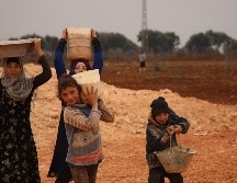 Varios niños transportan agua en recipientes improvisados, en un campo de refugiados sirios. AFP/A. Watad