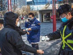 Medidas sanitarias. Personal de vigilancia de un centro comercial mide la temperatura de los visitantes en la capital china. AFP
