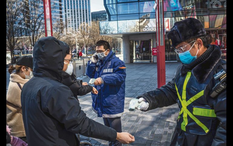 Medidas sanitarias. Personal de vigilancia de un centro comercial mide la temperatura de los visitantes en la capital china. AFP
