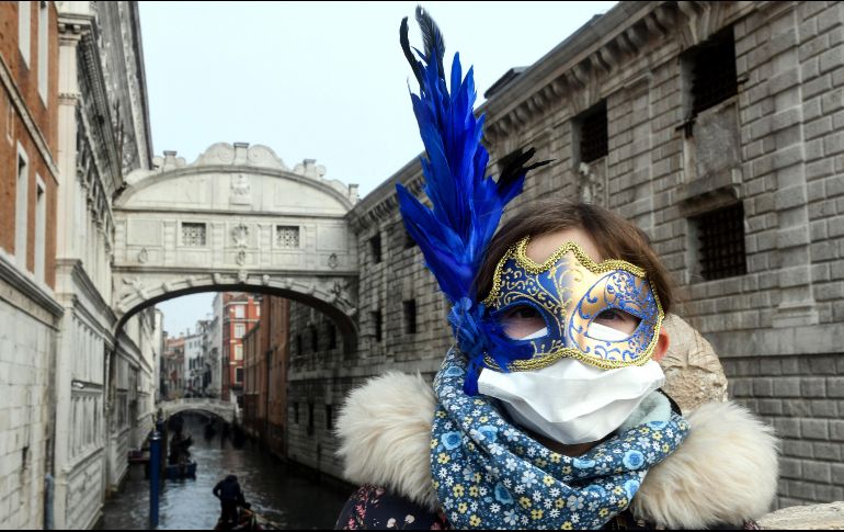 Un turista con máscara de carnaval usa hoy una mascarilla en Venecia. La ciudad suspendió las celebraciones del carnaval ante el brote del covid-19 en Italia. AFP/A. Pataro