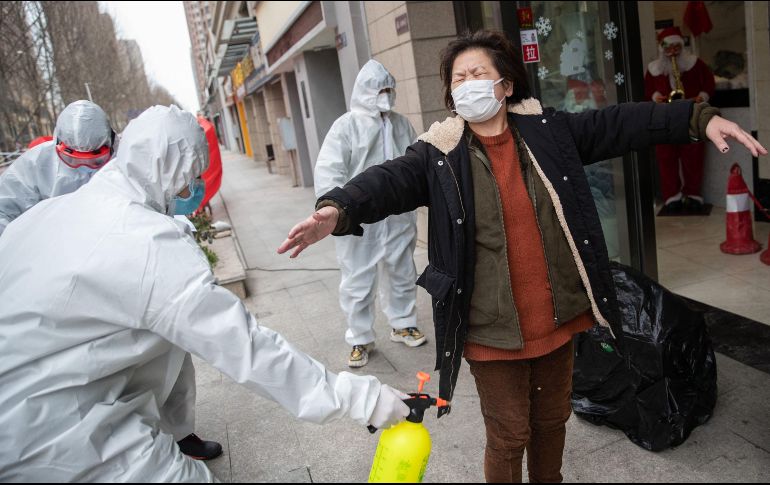 Voluntarios desinfectan a una mujer que se ha recuperado de covid-19 a su llegada a un hotel, donde estará en cuarentena por 14 días luego de recibir el alta de un hospital en Wuhan, China. AFP