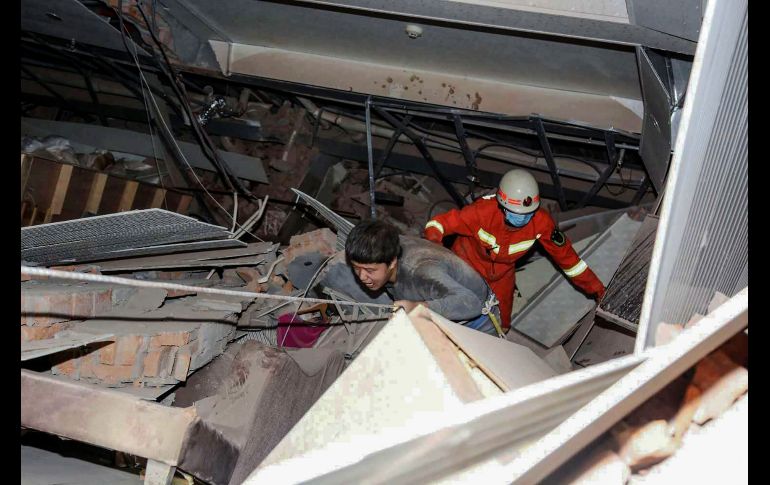 Trabajadores de rescate, vestidos con overoles anaranjados, trepan sobre escombros y estructuras metálicas retorcidas del hotel para sacar a las víctimas. AFP