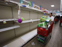 Los estantes de un supermercado en Nueva York lucen vacíos mientras una mujer los recorre con su carrito repleto de papel higiénico y otros artículos. AFP/A. Bello