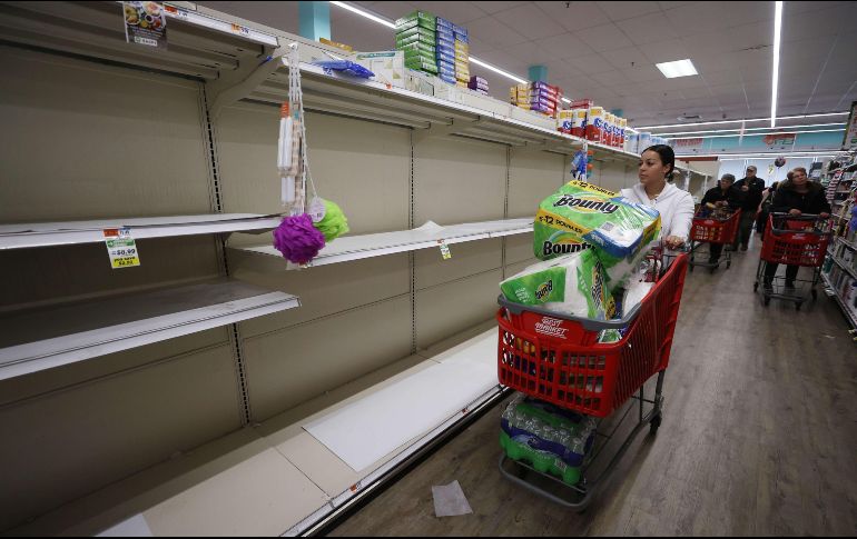 Los estantes de un supermercado en Nueva York lucen vacíos mientras una mujer los recorre con su carrito repleto de papel higiénico y otros artículos. AFP/A. Bello