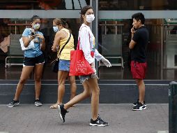 Una mujer camina por una calle donde varias personas hacen fila para comprar alimentos, este jueves en Lima. EFE/P. Aguilar