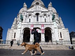 Un joven protegido con una mascarilla da un breve paseo a su perro por las calles semivacías de Montmartre. EFE/I. Langsdon