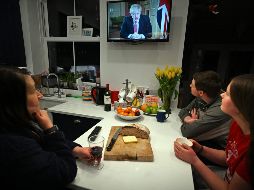 Una familia confinada en su casa ve en la televisión al primer ministro Boris Johnson ofrecer una conferencia de prensa. AFP/P. Ellis