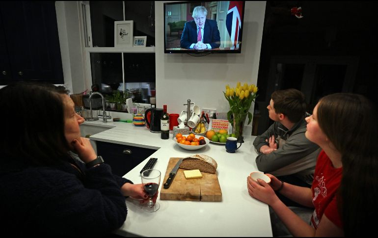 Una familia confinada en su casa ve en la televisión al primer ministro Boris Johnson ofrecer una conferencia de prensa. AFP/P. Ellis