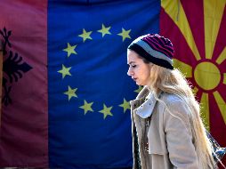 Una mujer camina frente a las banderas de Albania, la Unión Europea y Macedonia del Norte. EFE/G. Licovski