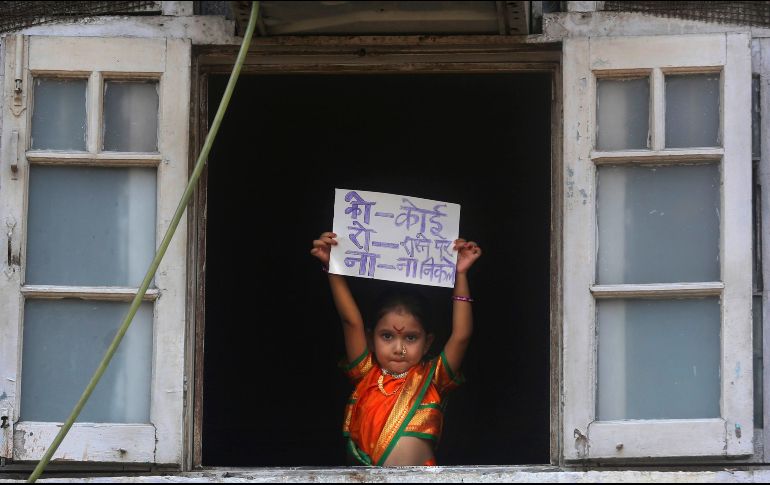 Una niña en atuendo tradicional para una celebración en la India muestra desde una ventana un letrero que dice 