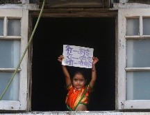 Una niña en atuendo tradicional para una celebración en la India muestra desde una ventana un letrero que dice 