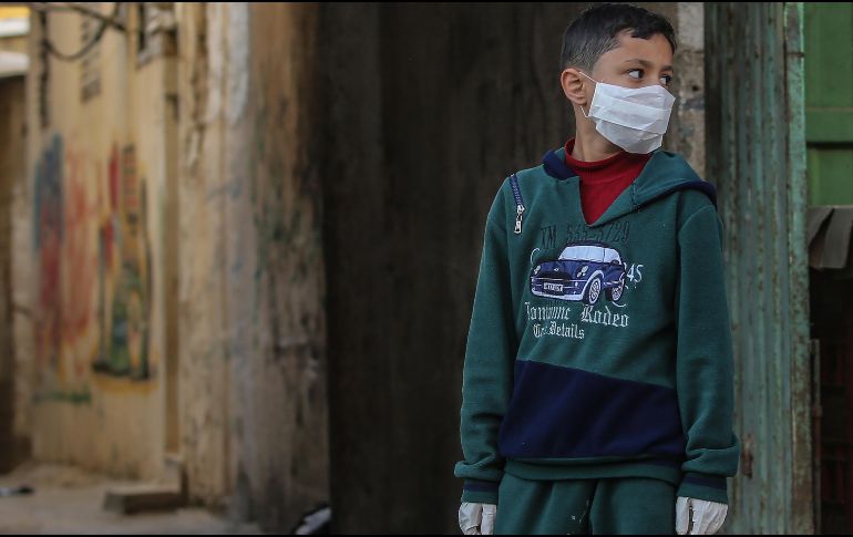 Un palestino usa una mascarilla protectora y guantes como medida de precaución contra la propagación del coronavirus, en calles del campo de refugiados de Al Shatea, en la Ciudad de Gaza. EFE/M. Saber