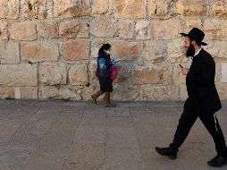 Una mujer con una máscara protectora y un hombre judío ortodoxo pasan cerca de las murallas de la ciudad vieja de Jerusalén. EFE/A. Sultan