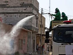 Trabajadores sanitarios aplican un líquido desinfectante a calles y viviendas de Iraq. AFP/H. Faleh