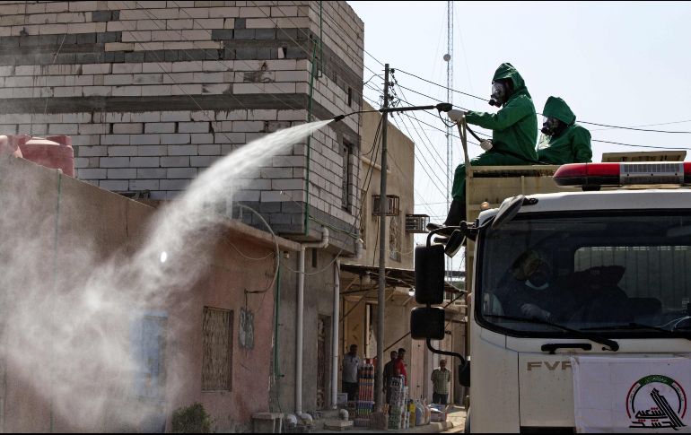 Trabajadores sanitarios aplican un líquido desinfectante a calles y viviendas de Iraq. AFP/H. Faleh