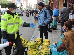 Un policía informa en un mercado sobre las restricciones decretadas por las autoridades bolivianas, este jueves en La Paz. EFE/L. Reglero