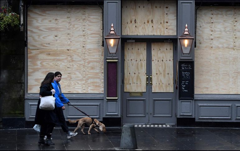 Dos personas pasean a su perro frente a un negocio cerrado como parte de las medidas de contención para evitar infecciones por COVID-19. AFP/A. Buchanan