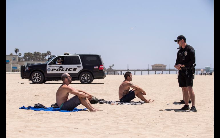 Un policía supervisa que jóvenes porten cubrebocas y los llama al distanciamiento mientras están en una playa de California. EFE / E. Laurent