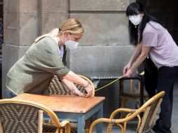 Unas trabajadoras toman medidas para instalar las mesas y que cumplan con las medidas de distanciamiento social en una terraza de la plaza Real. EFE/M. Pérez