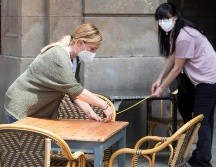 Unas trabajadoras toman medidas para instalar las mesas y que cumplan con las medidas de distanciamiento social en una terraza de la plaza Real. EFE/M. Pérez