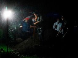 Bajo una fuerte lluvia, viento y truenos, los trabajadores de la funeraria se desinfectan y luego entregan un ataúd sellado a cuatro sepultureros. AFP/I. Ocon