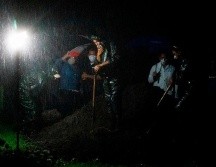 Bajo una fuerte lluvia, viento y truenos, los trabajadores de la funeraria se desinfectan y luego entregan un ataúd sellado a cuatro sepultureros. AFP/I. Ocon