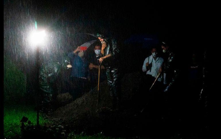 Bajo una fuerte lluvia, viento y truenos, los trabajadores de la funeraria se desinfectan y luego entregan un ataúd sellado a cuatro sepultureros. AFP/I. Ocon