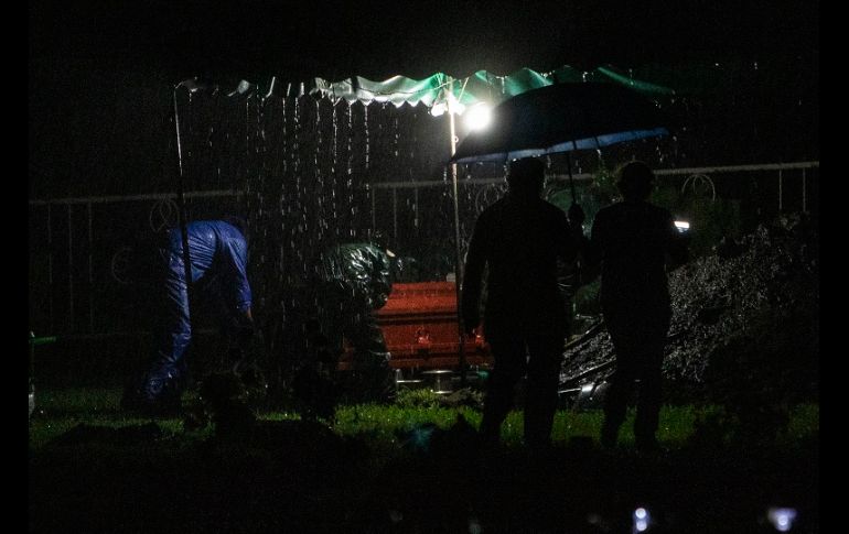 Bajo una fuerte lluvia, viento y truenos, los trabajadores de la funeraria se desinfectan y luego entregan un ataúd sellado a cuatro sepultureros. AFP/I. Ocon