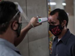 Un guardia mide la temperatura a un hombre que entra al Mercadao de Madureira, durante la segunda semana de reactivación decretada por el Gobierno local, en el norte de Río de Janeiro. EFE/A. Lacerda