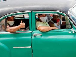 Varias personas con tapabocas pasean en un auto clásico por calles de La Habana. EFE/E. Mastrascusa
