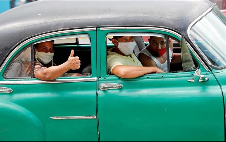 Varias personas con tapabocas pasean en un auto clásico por calles de La Habana. EFE/E. Mastrascusa