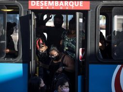 Pasajeros con mascarillas para prevenir la propagación del coronavirus descienden de un autobús hoy, en Río de Janeiro. EFE/A. Lacerda