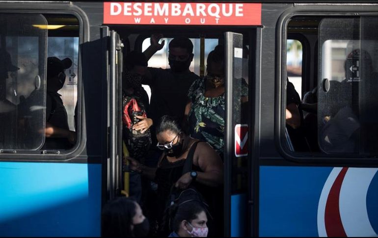 Pasajeros con mascarillas para prevenir la propagación del coronavirus descienden de un autobús hoy, en Río de Janeiro. EFE/A. Lacerda