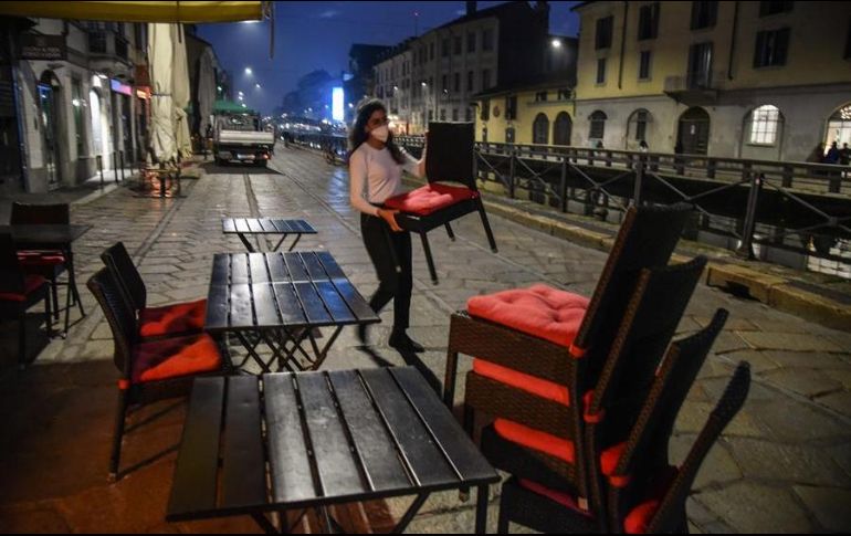 Una empleada de un restaurante recoge sillas y mesas previo a la hora del cierre, en Milan. EFE/M. Corner