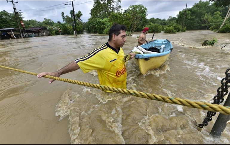 Dos personas tratan de cruzar una zona inundada por el desborde de los ríos hoy, en la sierra de Tabasco, otra región afectada por las lluvias. EFE/J. Avalos