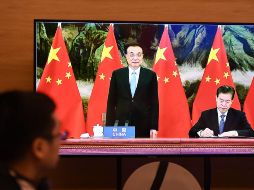 El primer ministro chino, Li Keqiang (c), y el ministro de comercio chino, Zhong Shan (d), durante la firma de la RCEP, en la ceremonia vista en una televixión en Hanói, Vietnam. La cumbre de 15 países se realizóde forma virtual por la pandemia. AFP/N. Nguyen