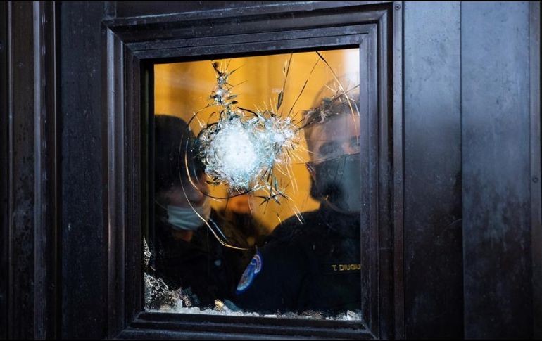 Policías observan desde un vidrio roto del Capitolio después del asalto a la institución por parte de manifestantes pro-Trump. EFE/M. Reynolds
