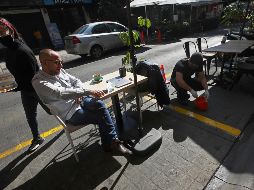 Un hombre come hoy mientras un trabajador marca una zona junto a una calle en la zona de Polanco, en Ciudad de México. AP/M. Ugarte