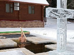 Putin, de 68 años, tras quitarse un grueso abrigo y las botas, con un traje de baño azul, entró en una piscina frente a una gran cruz translúcida, aparentemente tallada en el hielo y rodeada de nieve. AFP / Sputnik / M. Klimentyev