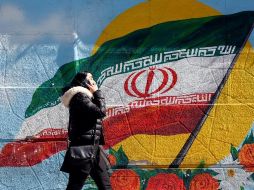Una mujer habla por teléfono mientras camina junto a una pintura mural de la bandera nacional en Teherán, Irán. EFE/A. Taherkenareh