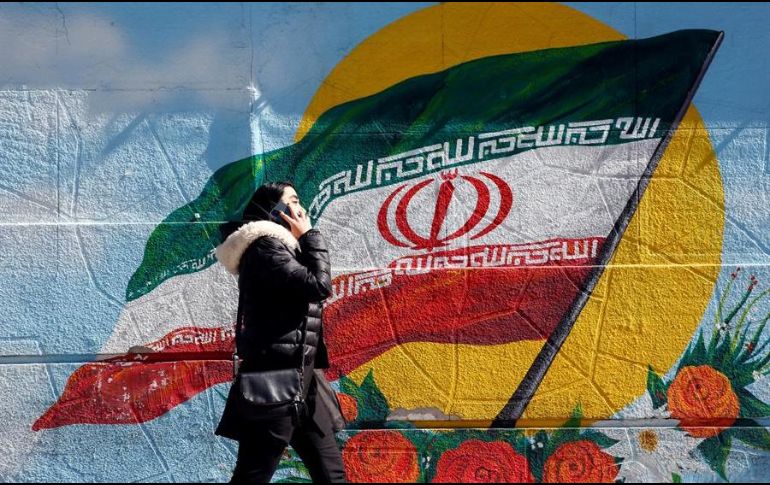 Una mujer habla por teléfono mientras camina junto a una pintura mural de la bandera nacional en Teherán, Irán. EFE/A. Taherkenareh