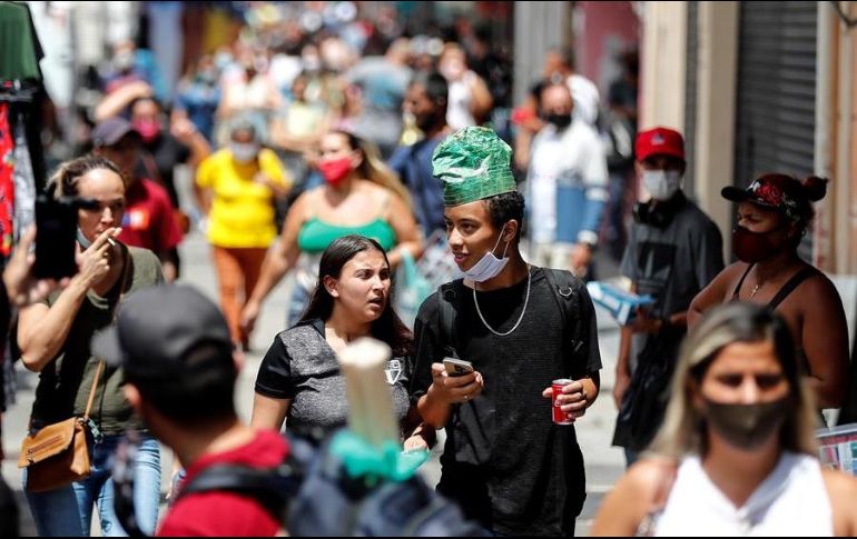 Dos jóvenes que no hacen uso correcto del tapabocas caminan en una concurrida calle comercial en Sao Paulo. EFE/S. Moreira