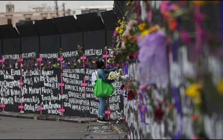 Una mujer coloca flores en las vallas metálicas afuera de Palacio Nacional junto a los nombres de víctimas de feminicidios. EFE / S. Gutiérrez