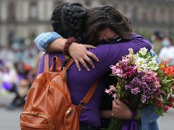 Dos mujeres se abrazan, junto a las cruces y carteles con nombres de víctimas por feminicidios instalados en las vallas metálicas afuera de Palacio Nacional. EFE / S. Gutiérrez