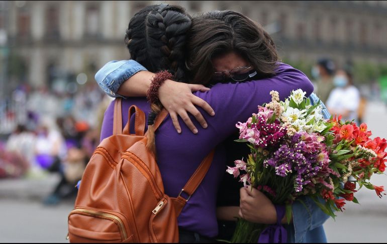 Dos mujeres se abrazan, junto a las cruces y carteles con nombres de víctimas por feminicidios instalados en las vallas metálicas afuera de Palacio Nacional. EFE / S. Gutiérrez