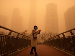 Una mujer camina por un puente peatonal durante la tormenta de arena en Pekín, China. AP/M. Schiefelbein
