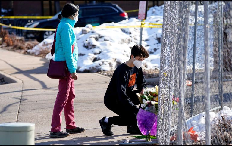 Un joven deja flores junto a una reja colocada alrededor del estacionamiento del supermercado donde ayer se registró el tiroteo en Boulder, Colorado. AP/D. Zalubowski