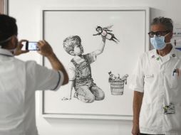 La pintura en blanco y negro muestra a un niño sentado en el piso jugando con una muñeca de enfermera superheroína. AP / ARCHIVO